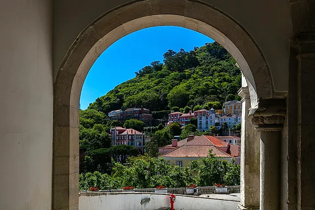 Looking through a stone arch of the National Palace of Sintra towards the wooded hill of the Castle of the Moors