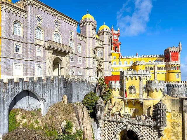 The colourful façade of Pena Palace, with yellow domes, patterned grey walls and a red tower