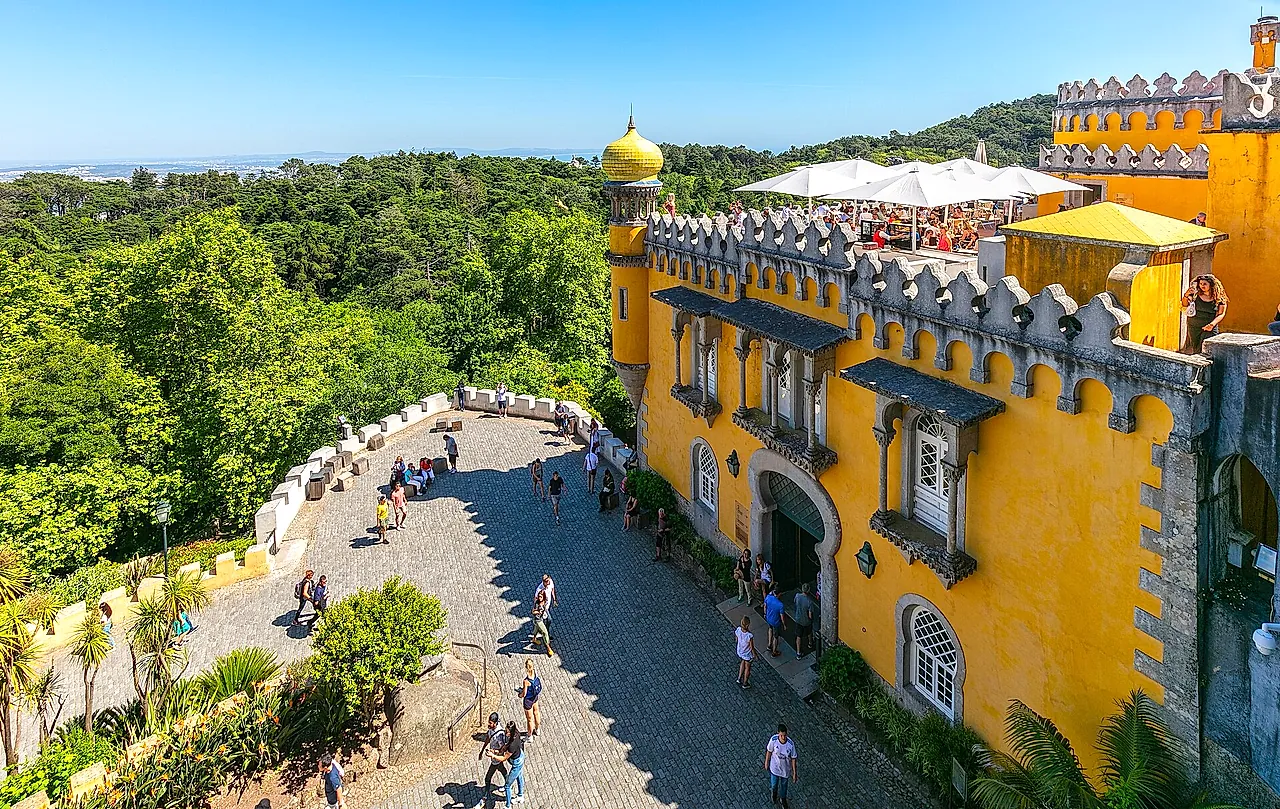 The yellow terrace of Pena Palace with its battlements and arches, above the green hills of Sintra