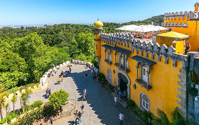 The yellow terrace of Pena Palace with its battlements and arches, above the green hills of Sintra