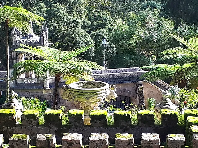 A carved stone fountain basin among ferns in the gardens of Quinta da Regaleira